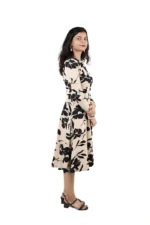 Woman in a beige and black floral midi dress, side view, with arms crossed