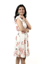 Woman in a white floral ruffle dress, angled side view, arm crossed, smiling