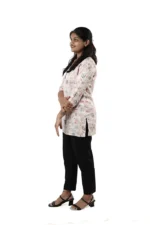 Woman in a white floral printed kurti with black pants, side view, standing and smiling