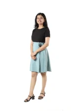 Woman in a black top and light blue skirt, side angle, standing and smiling