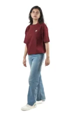 Woman standing sideways in maroon t-shirt and blue jeans.