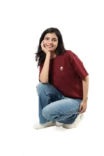 Woman crouching and smiling in maroon t-shirt and blue jeans.